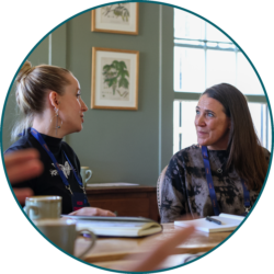 Two colleagues wearing conference lanyards engaged in a business discussion during a team meeting.